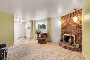 Living room featuring carpet, a fireplace, a ceiling fan, and a textured ceiling