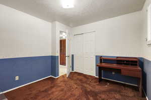 Unfurnished office featuring carpet, a textured ceiling, and wainscoting