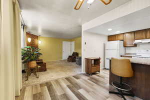 Kitchen featuring white appliances, under cabinet range hood, light wood finished floors, light countertops, and open floor plan