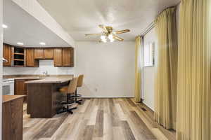 Kitchen with white range with electric stovetop, ceiling fan, a kitchen bar, light wood-style floors, and brown cabinets