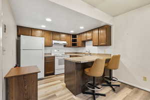 Kitchen with white appliances, under cabinet range hood, a peninsula, recessed lighting, and light wood-type flooring