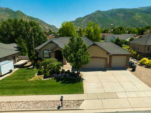 View of front facade with an attached garage, concrete driveway, a mountain view, a front lawn, and a shingled roof
