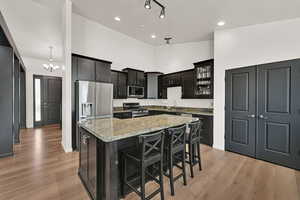 Kitchen featuring stainless steel appliances, light stone countertops, a kitchen island, a breakfast bar, and light wood-style flooring