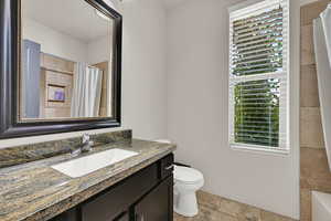 Bathroom featuring healthy amount of natural light, vanity, curtained shower, and stone tile flooring