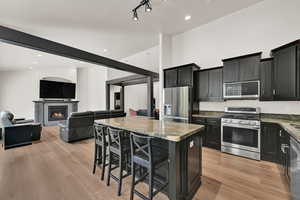 Kitchen featuring stainless steel appliances, dark cabinetry, a center island, stone countertops, and recessed lighting