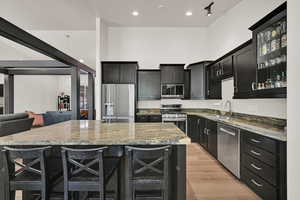 Kitchen with appliances with stainless steel finishes, dark cabinets, beverage cooler, a center island, and recessed lighting