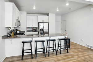 Kitchen featuring stainless steel appliances, a peninsula, new light wood-style LVP floors, a kitchen bar, and recessed lighting