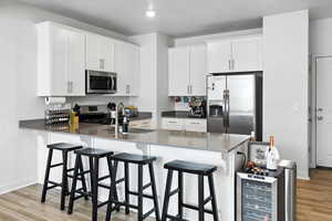Kitchen featuring stainless steel appliances, new light wood-style LVP floors, white cabinetry, a kitchen bar, and a peninsula