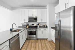 Kitchen featuring stainless steel appliances, new light wood-style LVP floors, white cabinetry, and dark grey quarts countertops