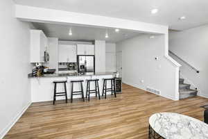 Kitchen featuring stainless steel refrigerator with ice dispenser, a peninsula, new light wood-style LVP floors, a breakfast bar area, and recessed lighting