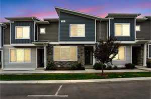 Dusk View of property featuring board and batten siding, stone siding, and uncovered parking
