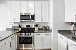 Kitchen featuring appliances with stainless steel finishes, white cabinets, and dark grey quarts countertops