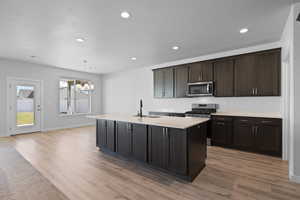 Kitchen with stainless steel appliances, light LVP floors, quartz countertops, and a kitchen island with sink