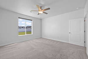 Primary bedroom featuring light colored carpet, a ceiling fan, and large window with automatic blinds