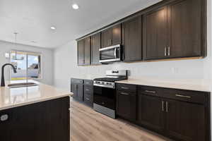 Kitchen with stainless steel appliances, light LVP floors, quartz countertops, and a kitchen island with sink