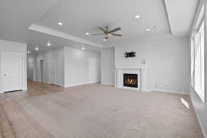 Unfurnished living room with a tray ceiling, light LVP floors, a ceiling fan, recessed lighting, and a tile-surround fireplace