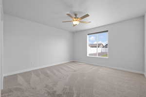 Primary bedroom featuring light colored carpet, a ceiling fan, and large window with automatic blinds