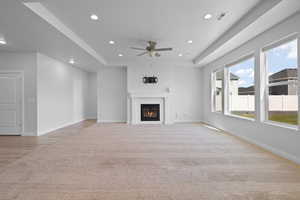 Unfurnished living room with a tray ceiling, light LVP floors, a ceiling fan, recessed lighting, and a tile-surround fireplace