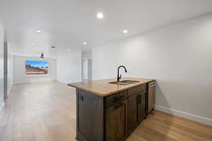Kitchen with dark brown cabinetry, light stone counters, light wood-style floors, stainless steel dishwasher, and recessed lighting