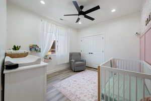 Bedroom featuring a crib, light wood-style floors, recessed lighting, a ceiling fan, and a closet