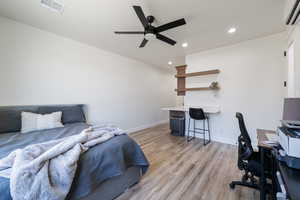 Bedroom with a wall mounted AC, recessed lighting, light wood-type flooring, an office area, and a ceiling fan