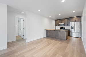 Kitchen featuring appliances with stainless steel finishes, dark brown cabinets, recessed lighting, a peninsula, and light wood-style flooring