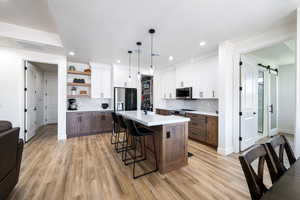 Kitchen featuring stainless steel appliances, a kitchen bar, light countertops, backsplash, and a barn door
