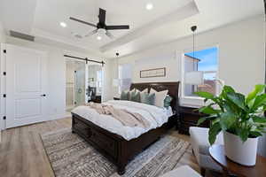 Bedroom featuring a tray ceiling, a barn door, light wood-type flooring, recessed lighting, and ensuite bath