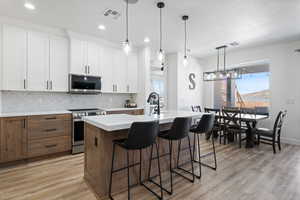 Kitchen featuring appliances with stainless steel finishes, light countertops, backsplash, a kitchen island with sink, and white cabinets