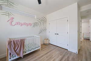 Bedroom featuring wood finished floors, a closet, a nursery area, and ceiling fan