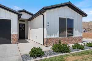 Doorway to property featuring board and batten siding, a garage, stone siding, and a tiled roof