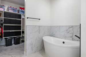 Full bathroom featuring a freestanding tub, marble finish floors, tile walls, and wainscoting