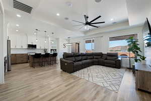 Living room with a tray ceiling, light wood-type flooring, a ceiling fan, and recessed lighting