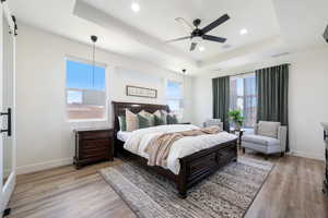 Bedroom with a tray ceiling, light wood-type flooring, recessed lighting, a barn door, and ceiling fan