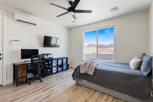 Bedroom with an AC wall unit, light wood-type flooring, an office area, and a ceiling fan