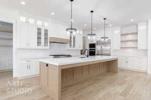 Kitchen featuring built in appliances, open shelves, backsplash, light countertops, and a large island with sink