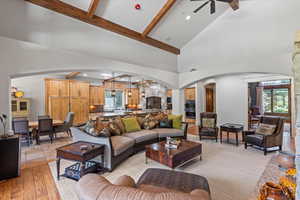 Living area featuring arched walkways, high vaulted ceiling, beamed ceiling, a ceiling fan, and light wood-type flooring