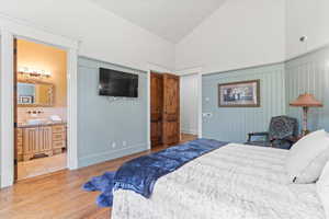 Bedroom with light wood finished floors, high vaulted ceiling, and ensuite bath