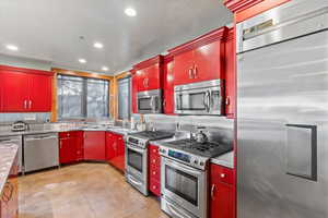 Kitchen featuring appliances with stainless steel finishes, red cabinets, stainless steel counters, tasteful backsplash, and recessed lighting
