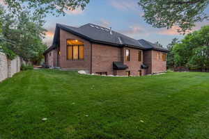 Back of property at dusk with brick siding, a yard, a shingled roof, and an attached garage
