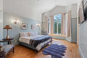 Bedroom featuring a decorative wall, wood-type flooring, and vaulted ceiling
