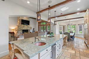 Kitchen featuring open floor plan, beam ceiling, recessed lighting, a fireplace, and stone tile floors