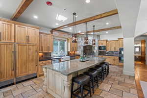Kitchen with black appliances, backsplash, beamed ceiling, a spacious island, and stone tile floors