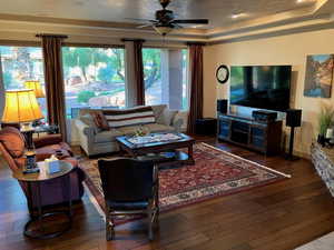 Living room with hardwood / wood-style flooring, a ceiling fan, and a raised ceiling