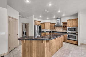 Kitchen with wall chimney range hood, stainless steel appliances, light tile patterned floors, a kitchen bar, and tasteful backsplash