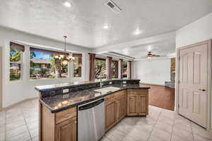 Kitchen with stainless steel dishwasher, a chandelier, light tile patterned floors, brown cabinetry, and a textured ceiling