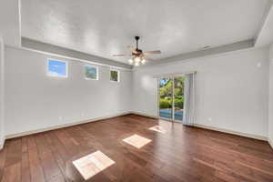 Empty room featuring ceiling fan, hardwood / wood-style flooring, a raised ceiling, and a textured ceiling