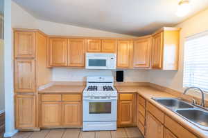 Kitchen featuring white appliances, lofted ceiling, light countertops, and light tile patterned floors