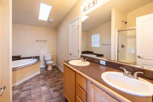 Bathroom with a skylight, a bath, a shower stall, double vanity, and lofted ceiling
