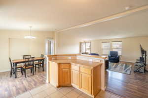 Kitchen featuring open floor plan, light wood-style floors, a chandelier, light countertops, and a kitchen island